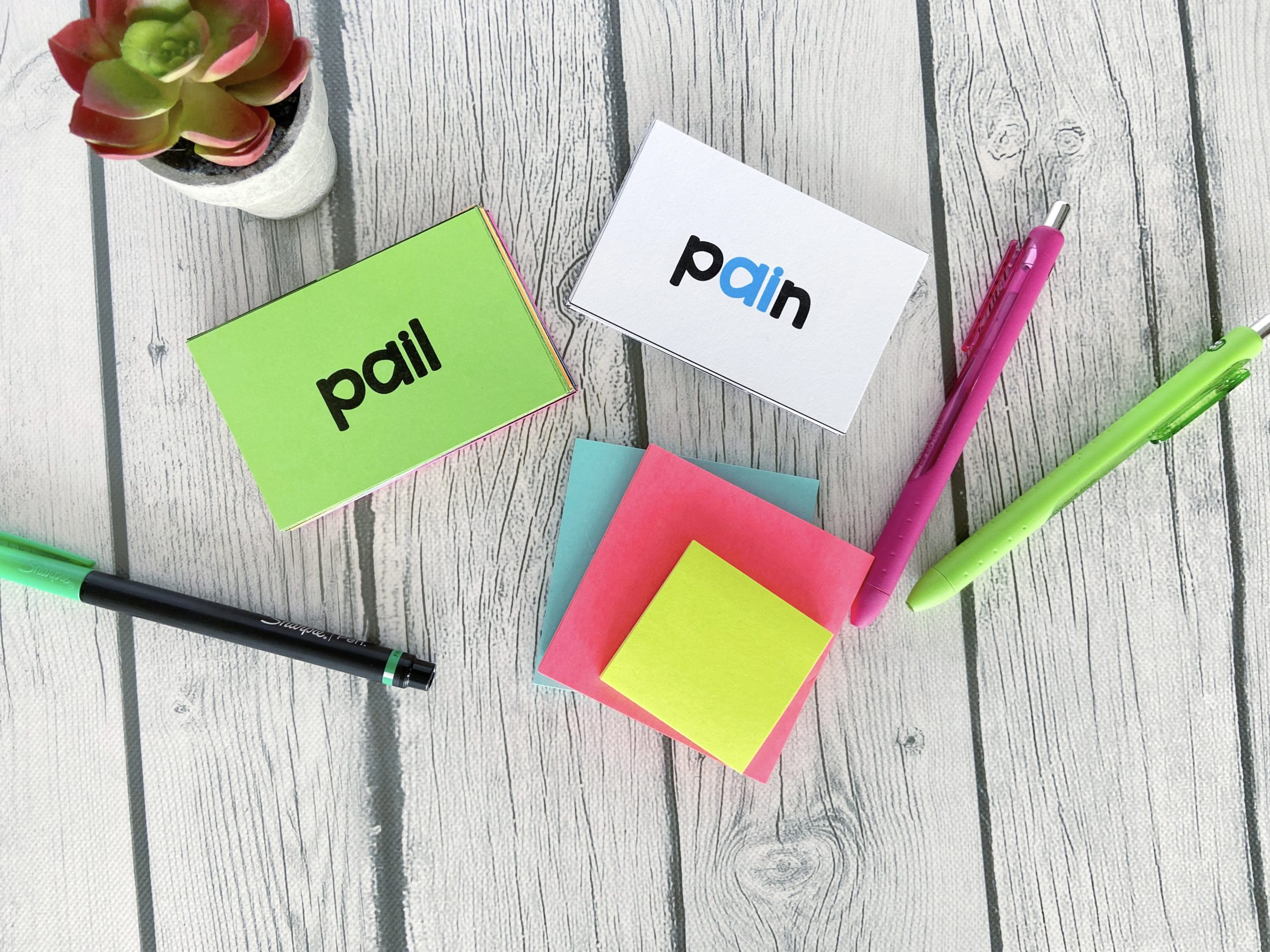 The words "pail" and "pain" on flashcards displayed with pens and sticky notes.